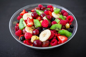 Fresh fruit salad in glass plate on dark background. Flat lay, top view