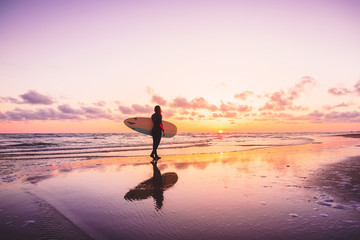 Surf girl with surfboard on a beach at colorful sunset. Surfer woman and waves