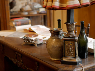 Vintage items, jug, bottle of wine, table lamp, inkwell, books and documents on the old desk.