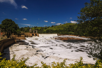 Fototapeta na wymiar A água poluída passando pela barragem, tendo como possível causa os esgotos sem tratamento liberados no rio em contraste com a bela paisagem