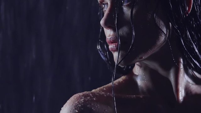mysterious girl with beautiful lips and big eyes standing in the dark in the shower. on the soft skin flowing water. she looks away and thought
