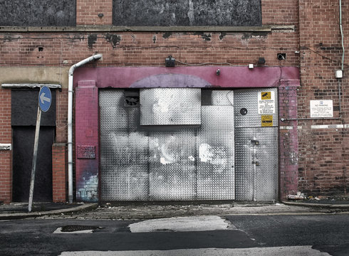derelict abandoned commercial property awaiting demolition or redevelopment with boarded up entrance and decaying brickwork in an empty road