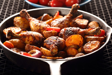 Roasted chicken legs with baked potato on frying pan