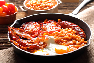 English Breakfast with sausages, grilled tomatoes, egg, bacon and beans on frying pan.