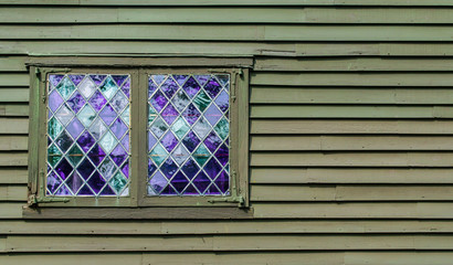 2 windows with purple panes in a leaded diamond pattern on the wall of a colonial building with...