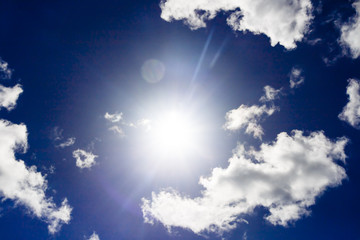 Naklejka na ściany i meble dramatic sun flare with fluffy clouds into deep blue sky, high contrast editing