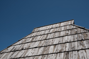 Old shake roof with weathered wooden planks and deep blue sky above