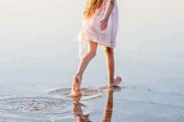 Happy beautiful girl running on water at sunset in dress and wreath
