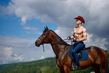 Macho man handsome cowboy and horse on the background of sky and water.