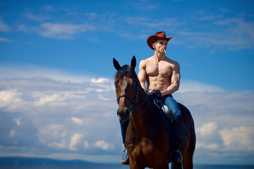 Macho man handsome cowboy and horse on the background of sky and water.