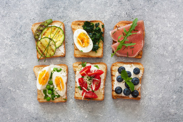 Assorted toasts with eggs, ham ,vegetables and fruits served on a gray stone background