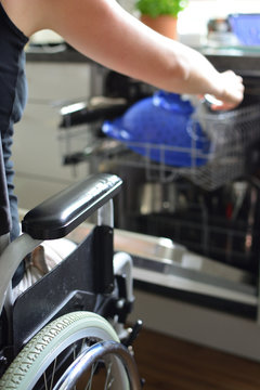 Junge Frau im Rollstuhl bedient Geschirrspülmaschine