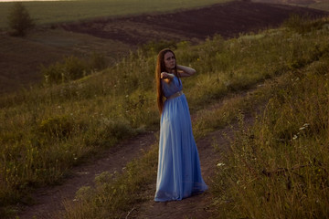 Fototapeta premium A girl in a long dress is walking on the road at sunset