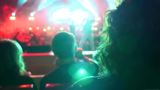 A crowd of people lit by colorful light during a concert of a rock band with a symphony orchestra. 4k. Slow motion