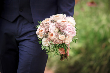 The groom holding a beautiful wedding bouquet of peonies