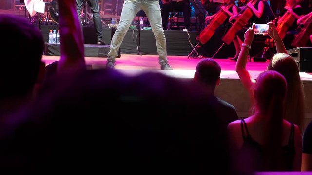 Viewers shoot video on smartphones during a concert of a rock band with a symphony orchestra. 4k