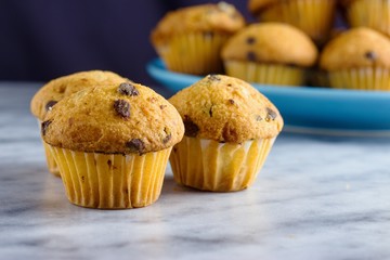 Chocolate chip mini muffins on marble surface in front of blue plate with some more muffins