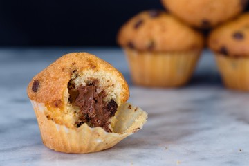 Small and half finished vanilla flavour muffin on marble surface. Several more muffins visible in background