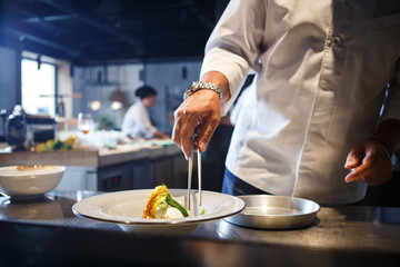 Food concept. Preparing traditional italian food. chef in white uniform decorate ready dish in interior of modern restaurant kitchen.