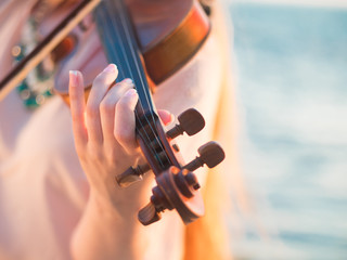 Young beautiful caucasian girl wearing jeans plays violin staying on the beach near the beautiful sea or ocean
