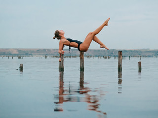 Young caucasian woman in swimsuit practicing yoga in water liman, lake or river. Beautiful reflection. Complex asanas, balance. Fitness, sport, yoga and healthy lifestyle concept.