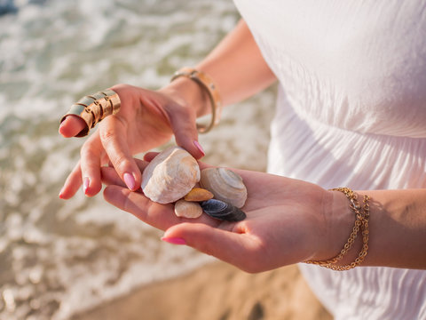 Hand holding sea shells and pumice stones found washed on rocky beach. close up hands with boho gypsy accessories. Woman standing on the beach at summer near sea.