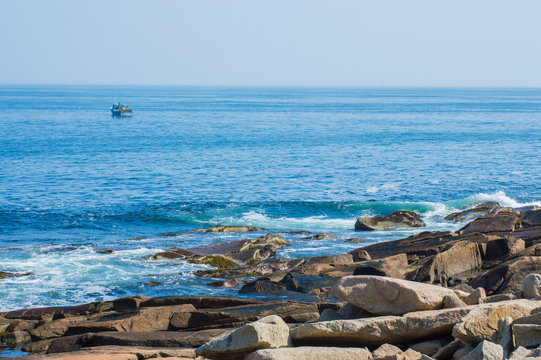 rocky coast of the Atlantic ocean with fishing boat in the distance at Cape Ann, Massachusetts