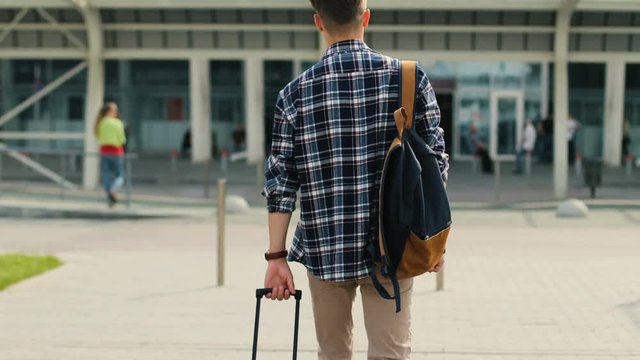 Young man walking to the modern airport terminal for his flight. View from the back.
