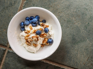 Ceramic bowl with yogurt, crashed walnuts and blueberries on a granite countertop