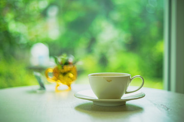 White cup of coffee on the table with morning sunlight and nature background