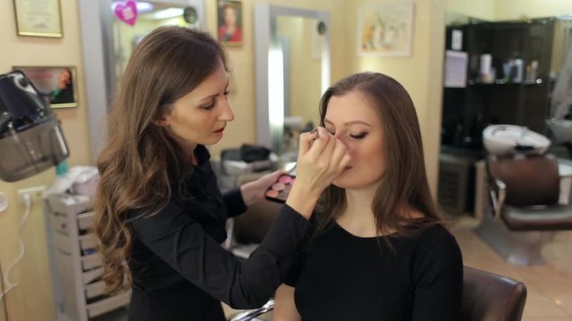Professional make-up artist doing make-up for the girl. Beauty salon. Beautiful woman face. Perfect make-up.