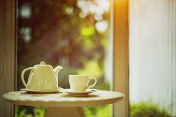 White cup of coffee on the table with morning sunlight and nature background