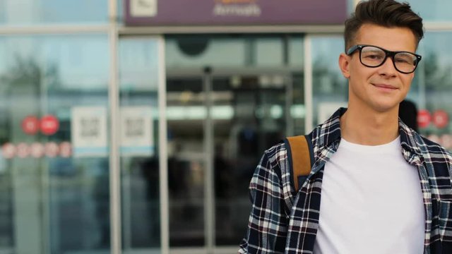 Young attractive man in the glasses walking from the modern airport terminal from his flight. Portrait shot.