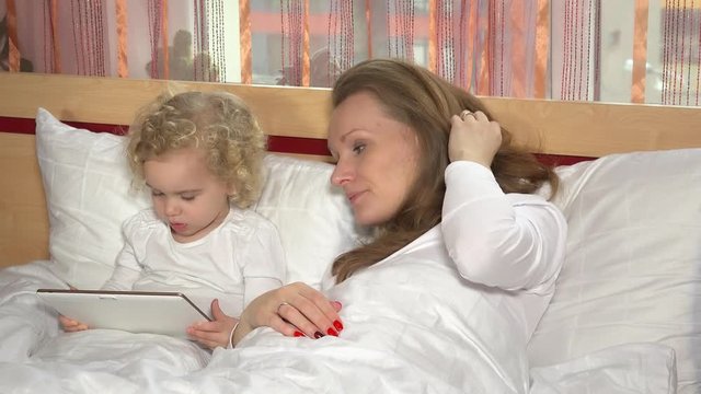 mother and toddler daughter in bed with tablet computer