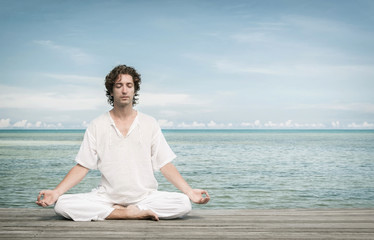 Fototapeta na wymiar Young man enjoying meditation in Lotus position on the beach.