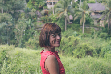 Naklejka na ściany i meble Young sexy woman in red dress in the tropical landscape of Bali island, Indonesia. Woman having summer vacation and enjoy paradise.