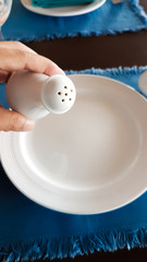 Man hand holding the ceramic of pepper bottle above the white dish