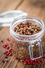 Wooden table with preserved Pink Peppercorns, selective focus