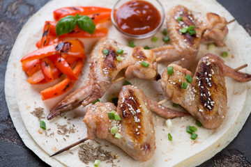 Skewers with barbecued chicken wings on tortilla wraps, horizontal shot, close-up