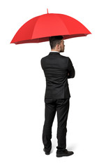 An isolated businessman standing with his back turned under a red umbrella.