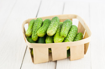 Lot of fresh green cucumbers in wicker basket on old white wooden background