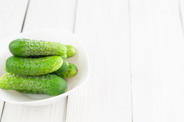 Lot of green fresh cucumbers in white bowl on rustic wooden background