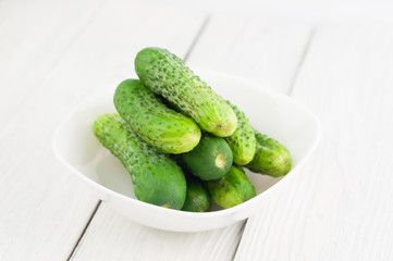 Lot of green fresh cucumbers in white bowl on rustic wooden background