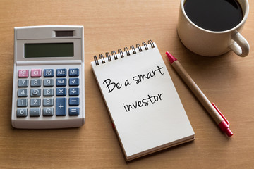 Be a smart investor, financial concept - handwriting on notepad with cup of coffee and calculator