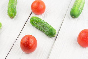 Three red ripe tomatoes and many fresh green cucumbers scattered on old wooden background