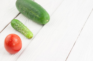 Red ripe tomato big and little fresh green cucumber on white rustic planks