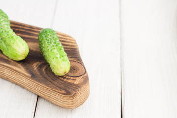 Fresh green cucumbers on rustic cutting board on old white wooden planks