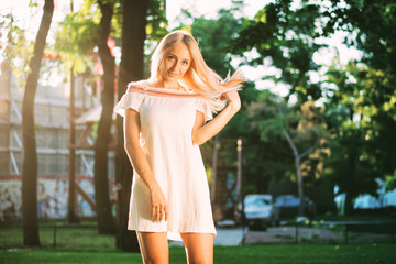 Naklejka premium Closeup Of Pretty Teen Blonde Girl In White Dress Smiling In The Park At Sunset. Greenery background.