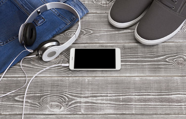 Jeans, smartphone, headphones shoes on a wooden background.