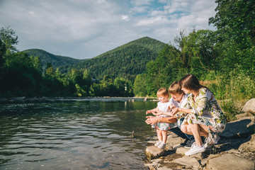 young family sits near mountain river with their daughter